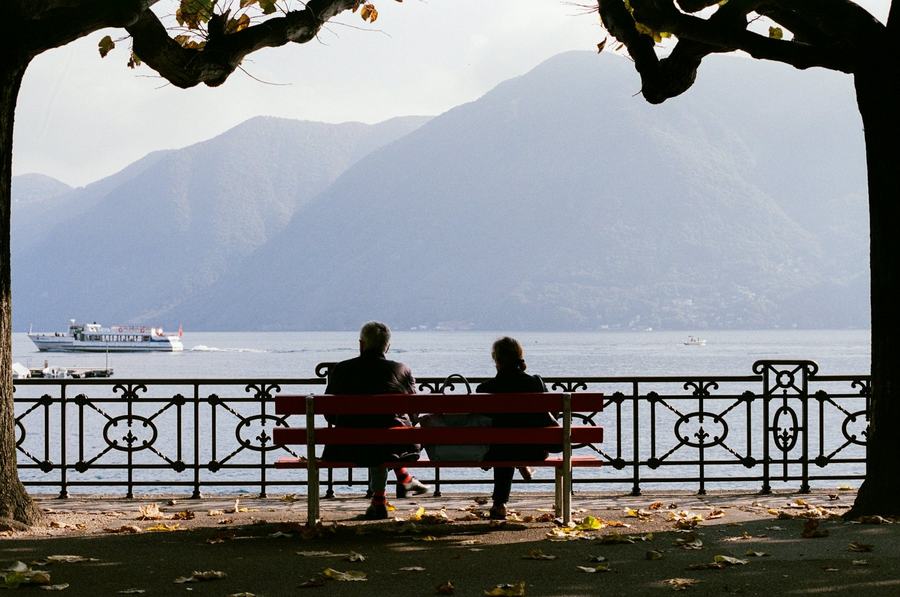 Una coppia su una panchina affacciata su un lago e le montagne in autunno